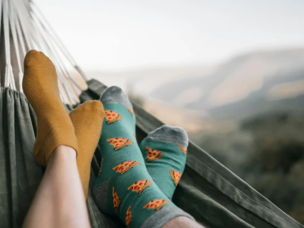 Pareja relajándose en una hamaca al aire libre, mostrando calcetines coloridos con diseños creativos.