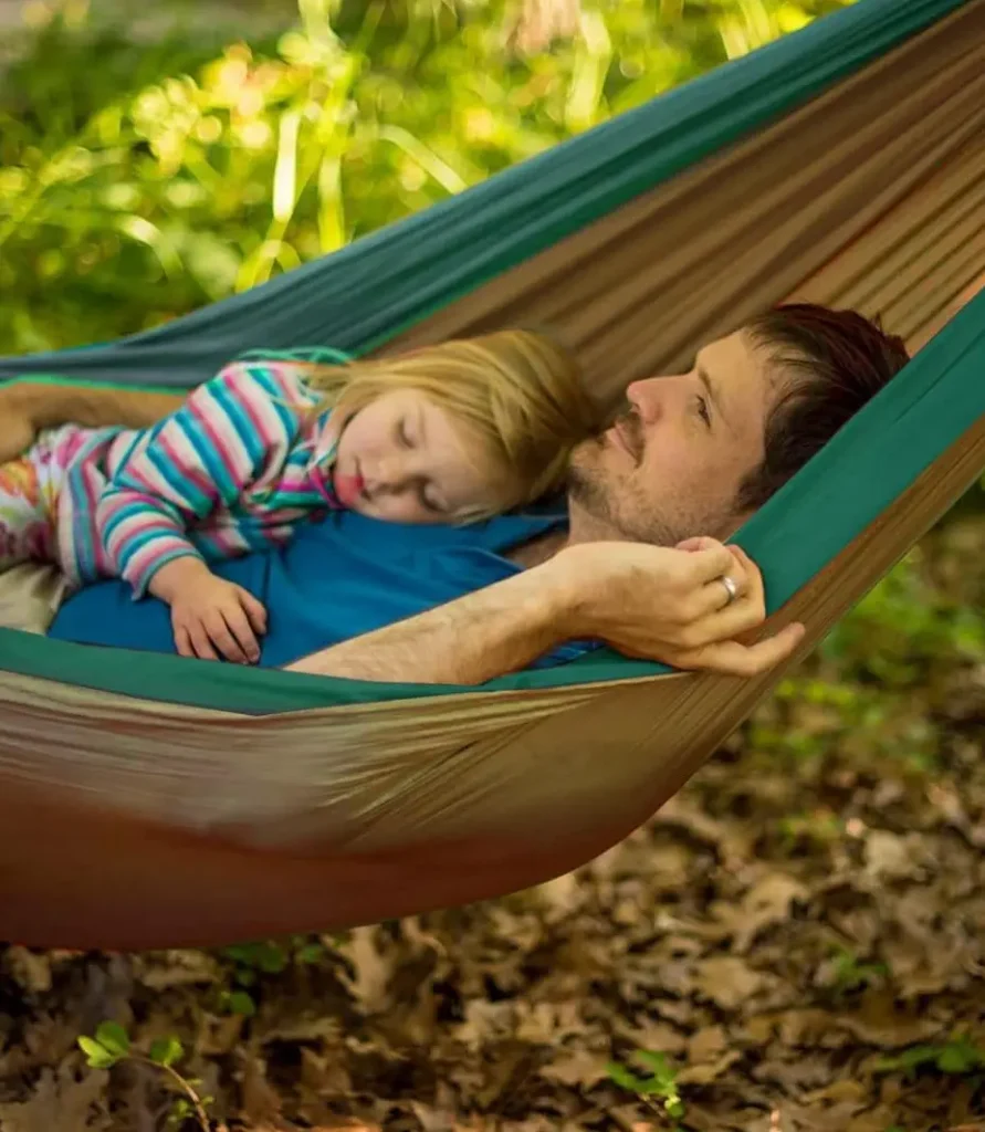 Hombre y niña durmiendo en una hamaca entre árboles en un entorno natural