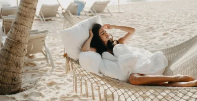Mujer relajándose en hamaca de red bajo una palmera en la playa, disfrutando del sol y el mar.