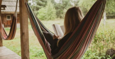 Mujer leyendo un libro mientras se relaja en una hamaca colorida en un entorno natural.