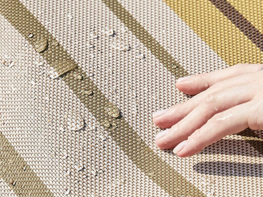 Mano sobre tela impermeable de una hamaca a rayas beige y verdes con gotas de agua.