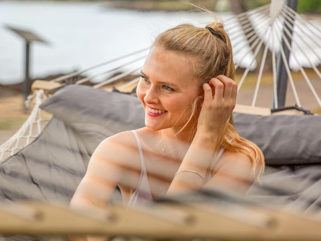 Mujer sonriendo mientras se relaja en una hamaca acolchada cerca de la playa.