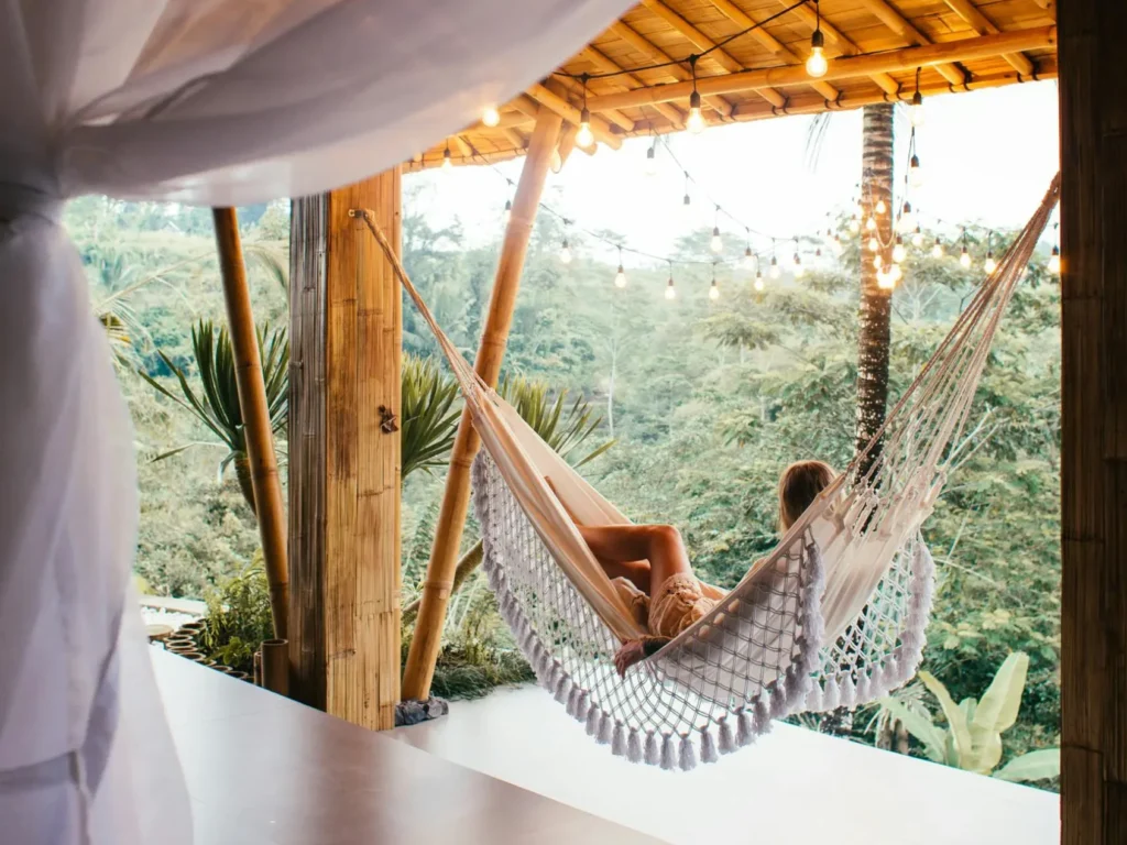 Mujer descansando en una hamaca tejida de macramé en una terraza tropical con techo de bambú.