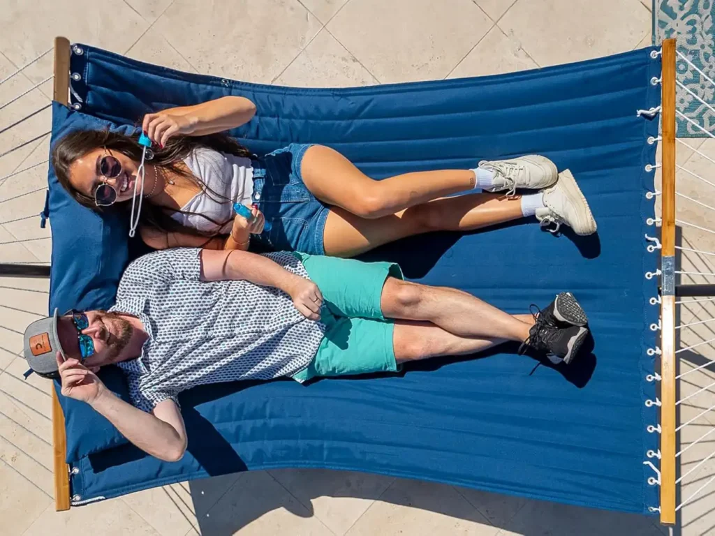 Pareja acostada en una hamaca azul disfrutando del sol en un día cálido junto a la piscina.